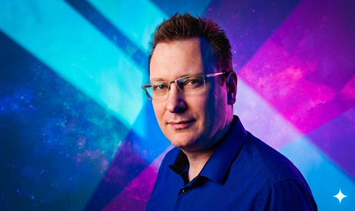 Ein Mann mit Brille und blauem Hemd vor einem farbenfrohen, kosmischen Hintergrund.